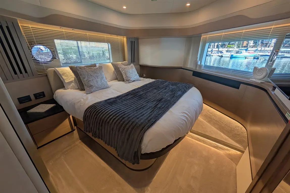 Spacious bedroom on a yacht featuring a double bed with grey throw, decorative pillows, and scenic views through large windows.